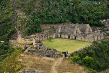 a castle on top of a lush green field with Choquequirao in the background